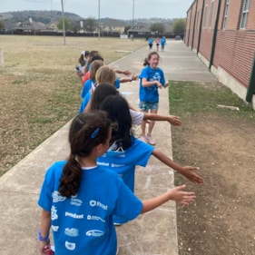 Girls on the Run participants smile while teammates give high five at the camera while running at an outdoor practice in blue shirts